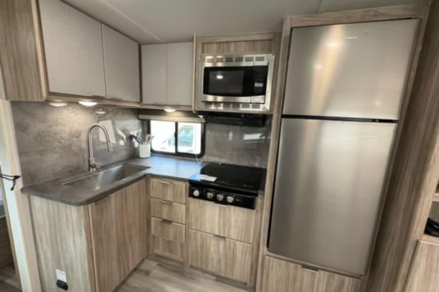 This modern rv rental kitchen offers a stainless steel sink, stovetop, microwave, and a spacious refrigerator.