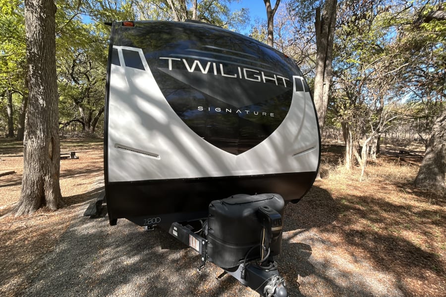 Black & white Twilight Signature 2800 travel trailer rv rental parked in a sunny, treed campground site.