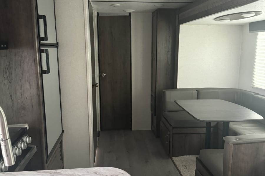Modern RV rental interior with a functional kitchen, comfortable dining booth, and a clear hallway layout.