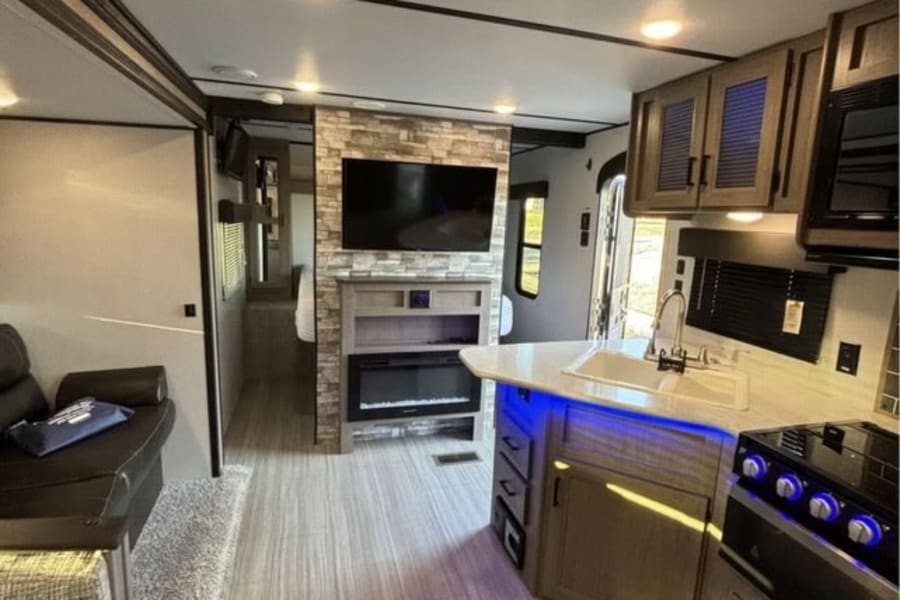 Explore this modern RV rental's spacious interior, featuring a cozy living area with a stone fireplace and a functional kitchen.