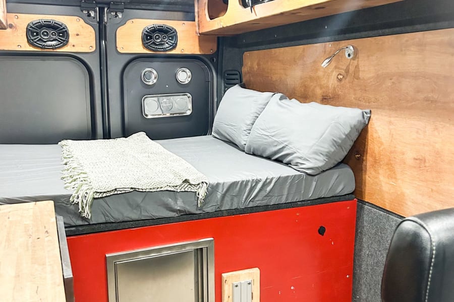 This RV rental offers a cozy bed, kitchen sink, and smart storage in a wood-paneled, custom camper van.