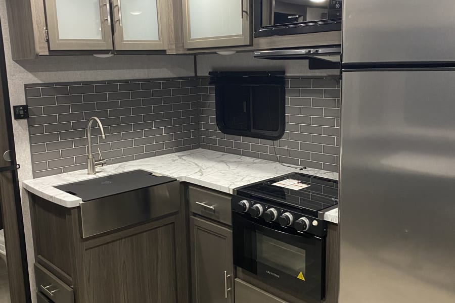 Modern RV rental kitchen with stainless steel appliances, grey backsplash, and marble countertops, perfect for your next adventure.