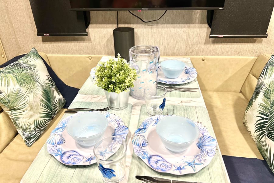 Enjoy an RV rental! Cozy dining area with ocean-themed table setting, pitcher, and cushions. Compact living space.