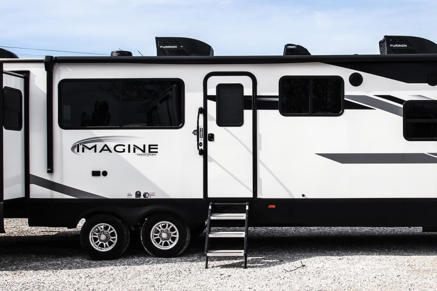 White Grand Design Imagine travel trailer RV rental, featuring geometric black and white graphics on a gravel lot.