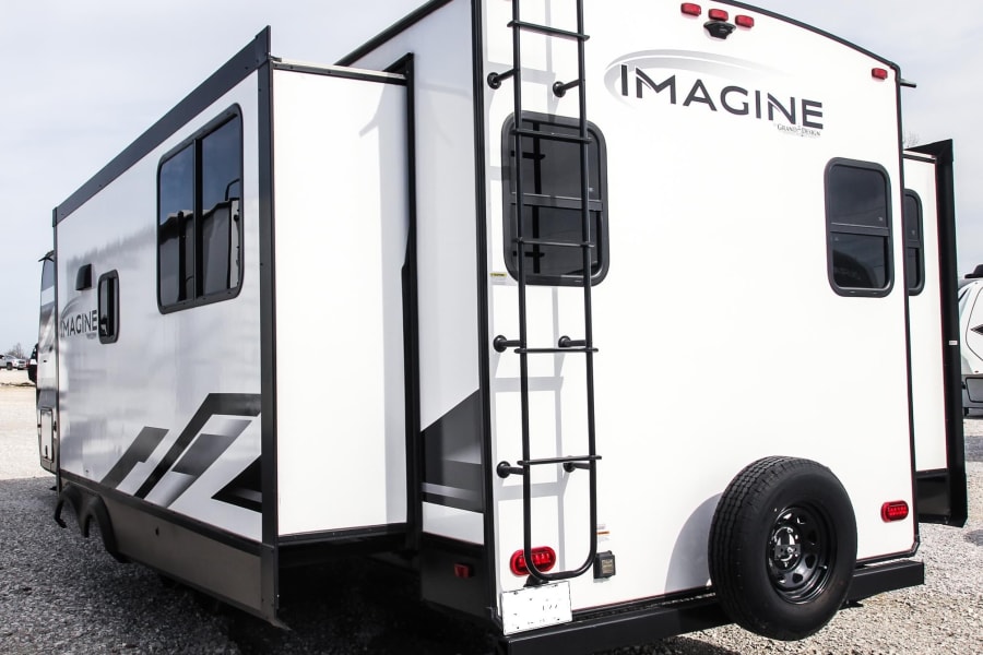 This white Imagine travel trailer RV, featuring extended slide-outs and a rear ladder, is ready for your next RV rental.