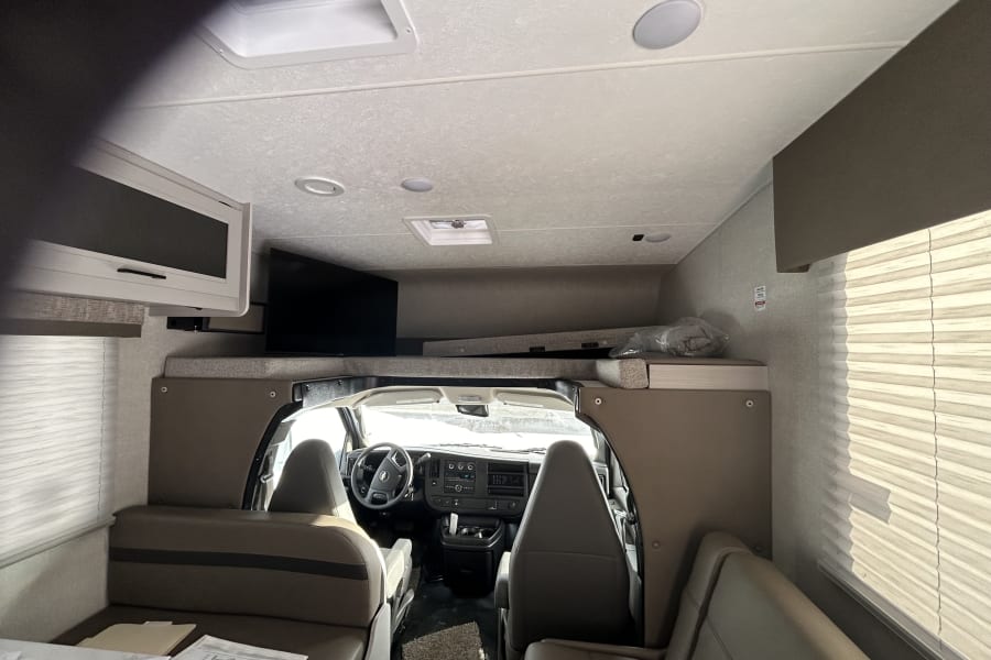 RV rental interior: Front cockpit with steering wheel, overhead bunk, TV, and living area seating visible. Ready for travel!
