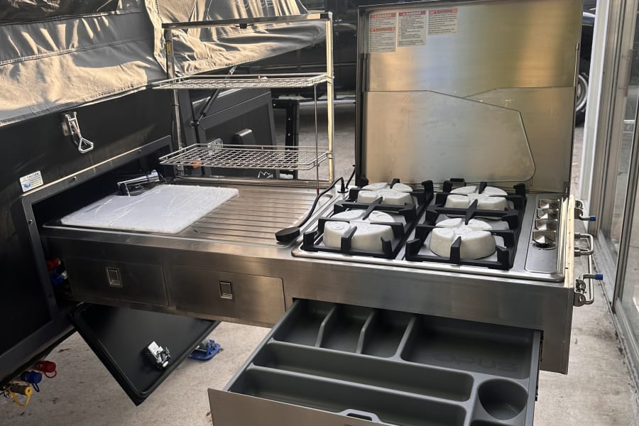 An Opus **RV rental** pop-up camper's outdoor kitchen with a gas stove and sink pulled out.