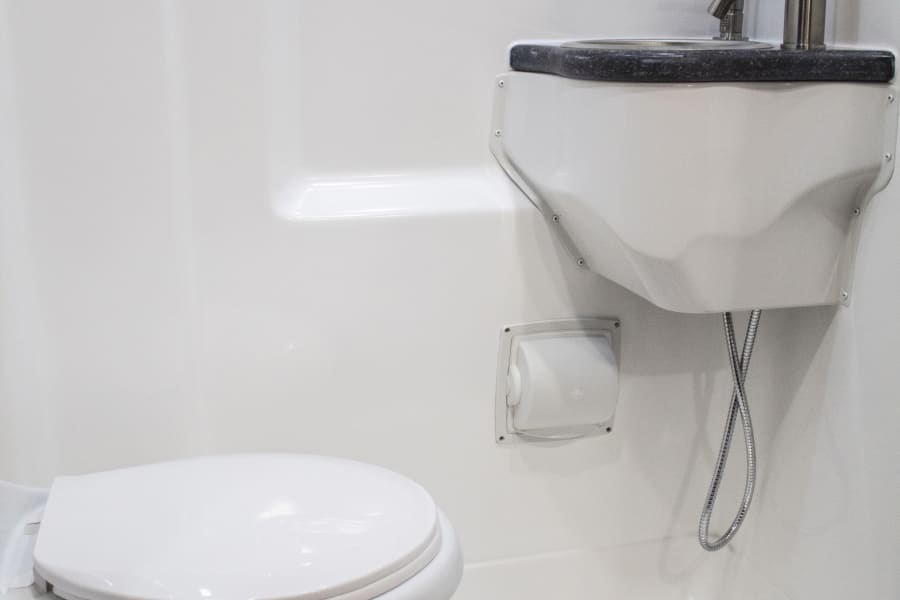 Compact RV rental bathroom: includes a toilet, sink, and shower in a white all-in-one design.