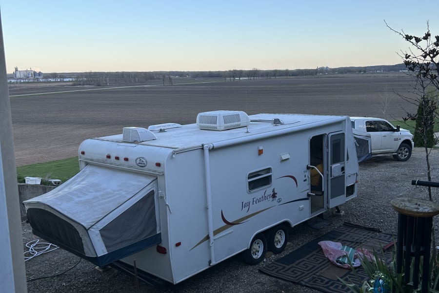 Jayco Jay Feather RV rental parked on gravel, with a pop-out bed, overlooking vast farmland and distant silos.