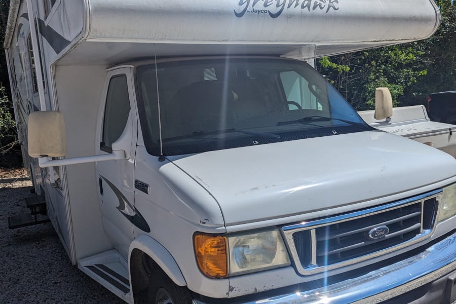 Sunny white Jayco Greyhawk Class C motorhome parked on gravel, ideal for rv rental adventures.