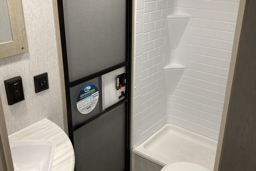 Modern RV rental bathroom features a compact sink, interior door, bright white shower, and toilet with patterned floor.