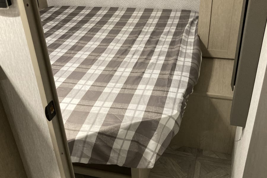 Cozy RV rental bedroom with plaid bedding and integrated storage.