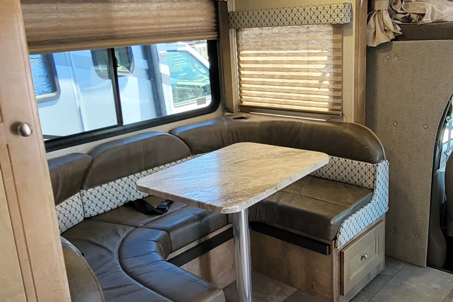 An RV rental interior featuring a spacious U-shaped dinette, table, and windows with blinds, offering cozy travel.