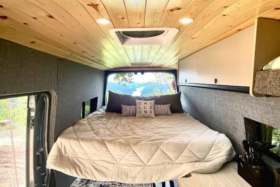 Explore this spacious RV rental interior: wood ceiling, elevated bed, lower sleeping, compact kitchen, & scenic lake view.