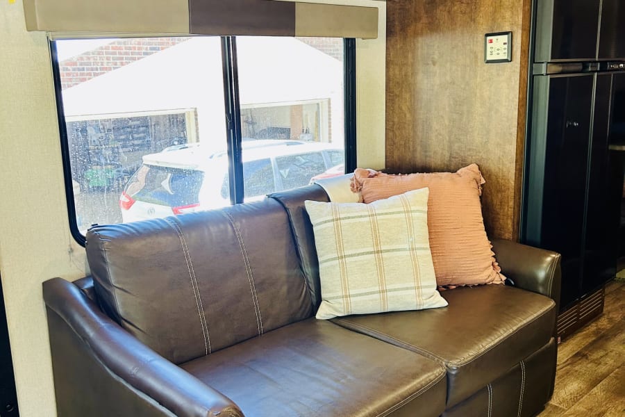 Cozy RV rental interior with a brown leather sofa, wood cabinets, and bright window, perfect for your next adventure.