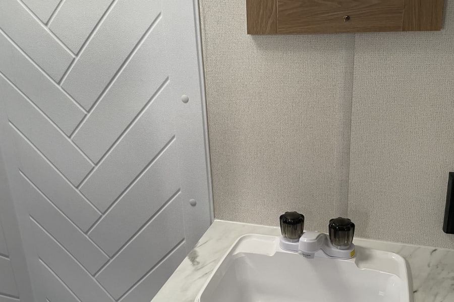 RV rental bathroom: compact vanity with sink & herringbone shower. Mirror reflects occupant.