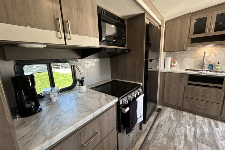 RV rental kitchen: light wood-grain cabinets, marble countertops, stove, microwave, and full-size refrigerator.