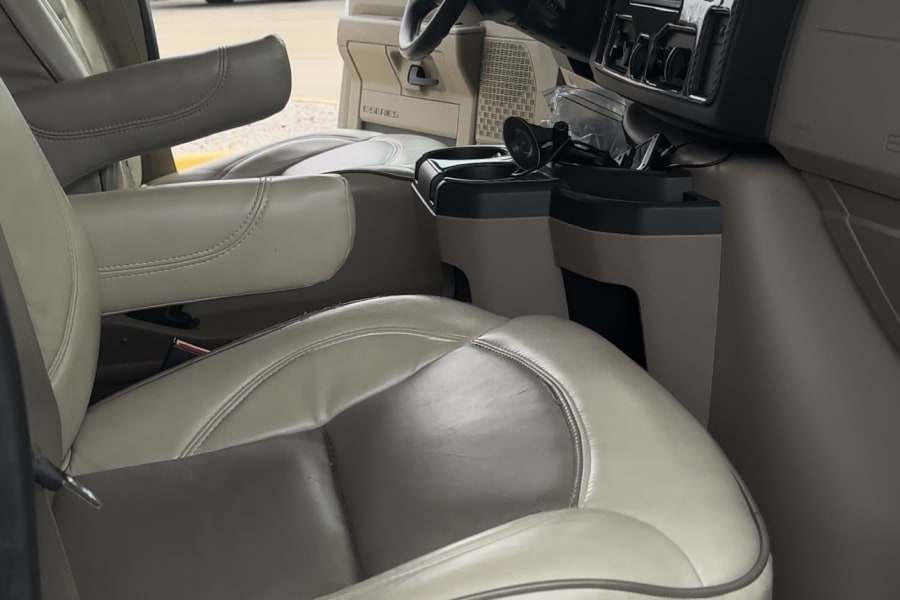 Inside an RV rental: light-colored leather front seats, armrests, and dashboard. Another RV is visible outside.