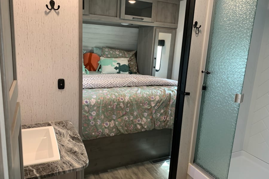 Inside an RV rental: view of a bedroom with floral bed, an adjacent sink, and a frosted glass shower stall.