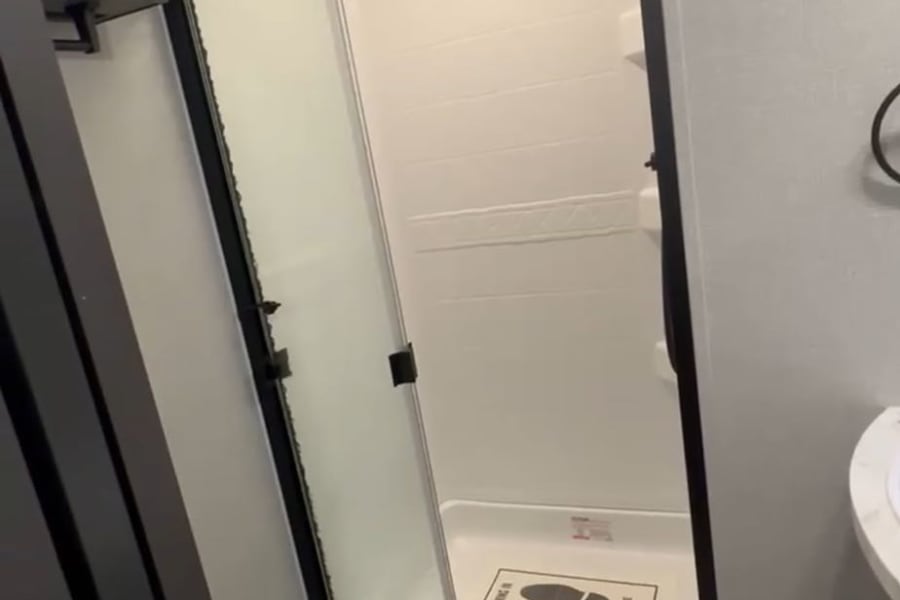 Inside an RV rental bathroom, featuring a clean white toilet, shower with a glass door, and a welcome mat.