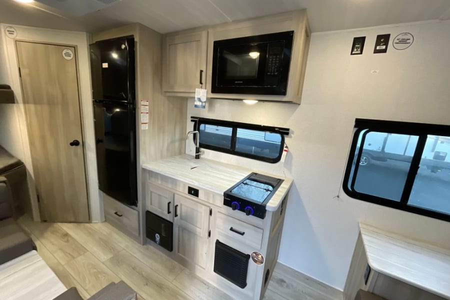 Bright RV rental interior featuring a compact kitchen with microwave, fridge, sink, and stovetop, perfect for travel.