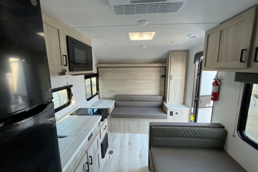 Spacious modern RV rental interior with a compact kitchen, comfortable convertible seating, and overhead storage.
