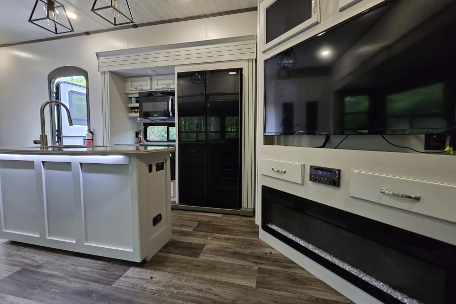 Spacious RV rental interior: modern kitchen with island, full-size fridge, and living area with TV & fireplace.