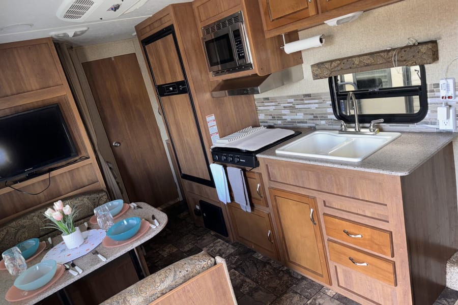 Cozy RV rental interior showcasing a well-equipped kitchen with microwave, stove, sink, fridge, dining area, and TV.