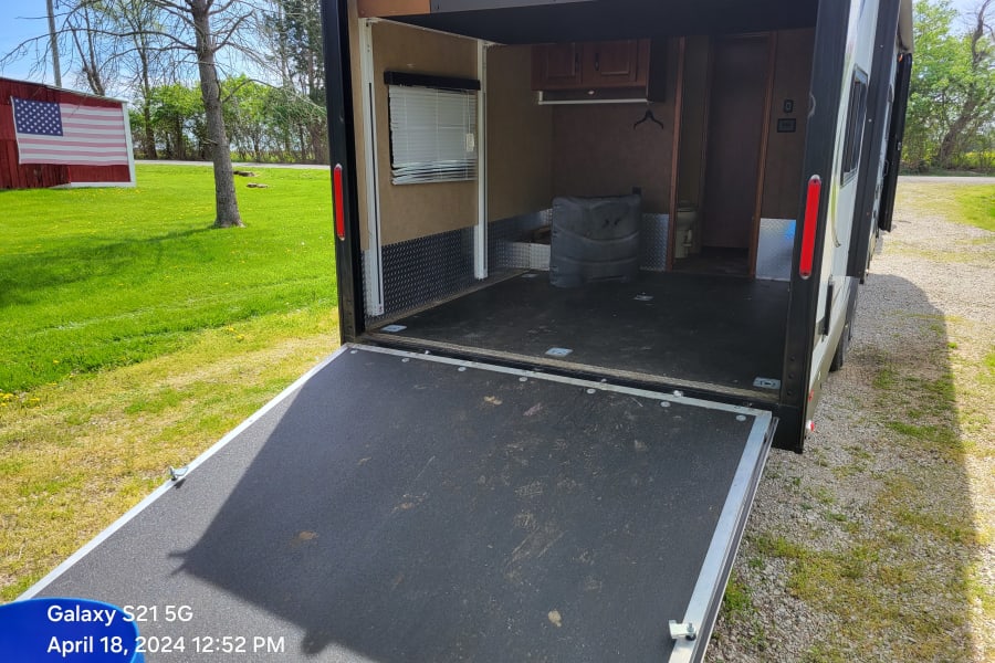Open toy hauler rv rental showing ramp, spacious interior with window, cabinets, and toilet. Ready for gear!