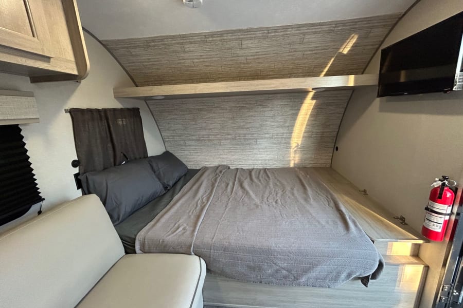 This RV rental bedroom offers a cozy bed, overhead storage, and TV, ideal for comfortable travel.