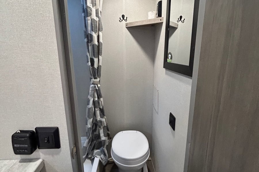 RV rental's compact bathroom: view shows toilet, shower with patterned curtain, and wall-mounted mirror.