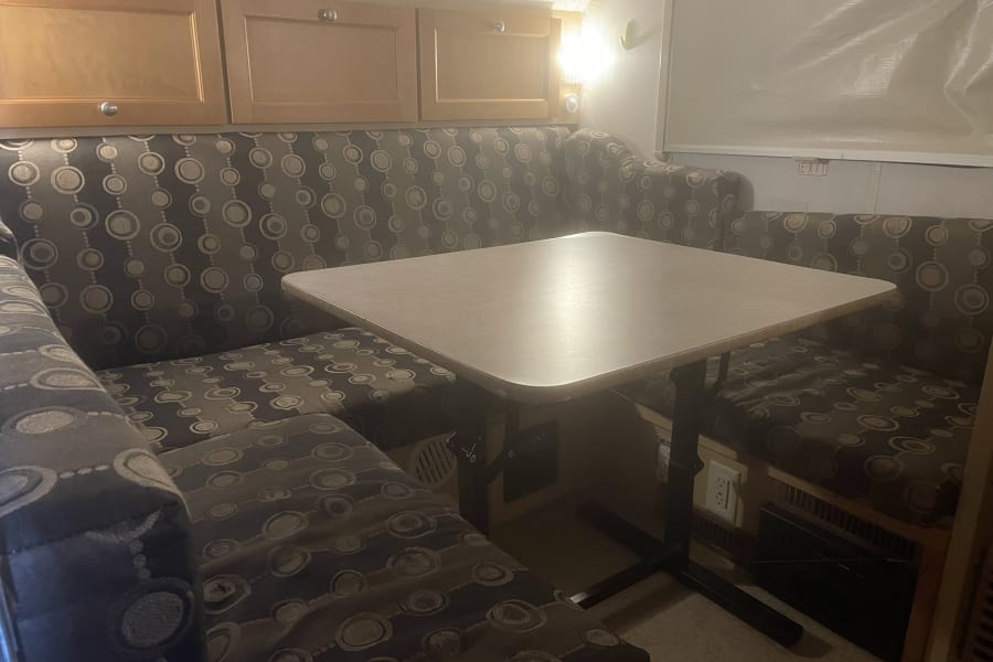 Cozy RV rental dinette features patterned cushion benches, a light-colored table, and wooden overhead cabinets.