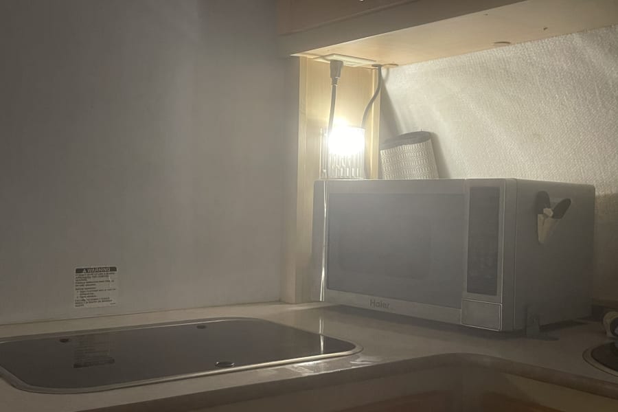 An RV rental galley features a compact kitchen with a flush cooktop/sink cover, a Haier microwave, and under-cabinet lighting.