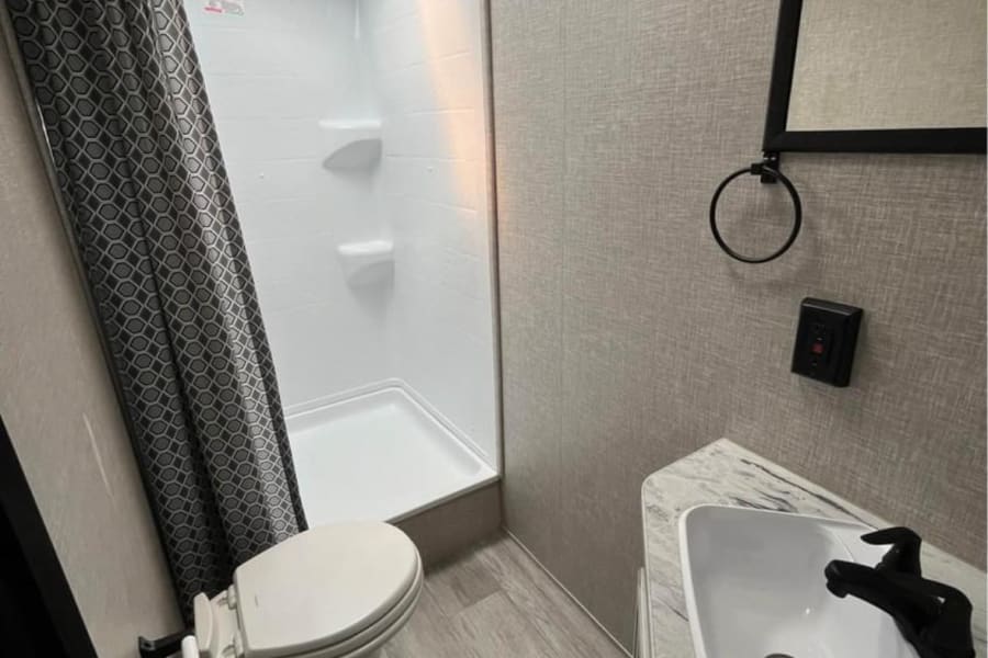 Modern RV rental bathroom with a compact shower, toilet, and sink vanity. Features a skylight and light-colored interior.