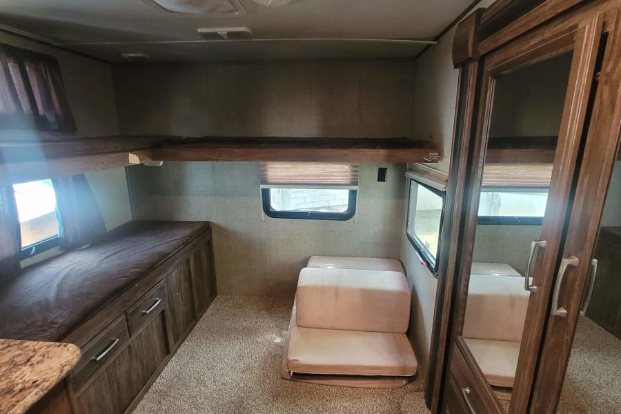 RV rental interior shows bunk beds, a folding mattress, and a mirrored cabinet, providing diverse sleeping arrangements.