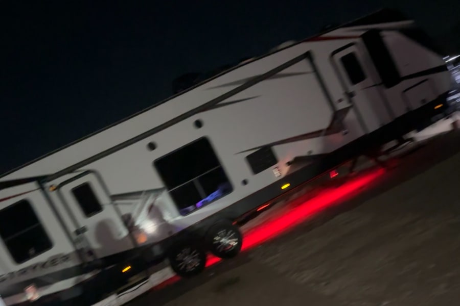 A large white Stryker RV rental, a travel trailer with red underglow lights, is parked at night.