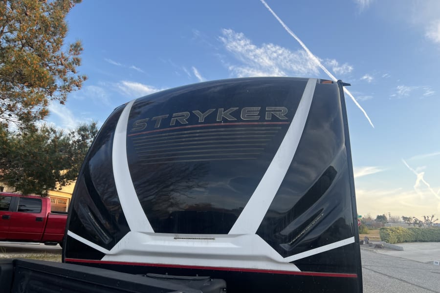 Stryker RV rental: Rear of this black & white toy hauler reflects trees & blue sky. Truck bed in foreground.