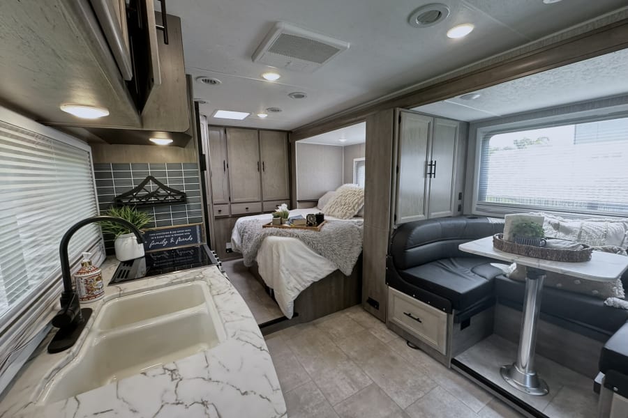 This modern RV rental interior features a full kitchen, cozy bedroom, and comfortable dinette, perfect for travel.