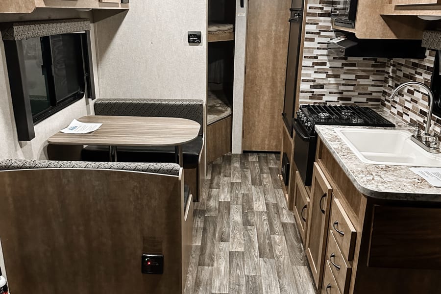 Inside an RV rental, discover a bright kitchen, dinette area, and bunk beds, with wood-look flooring.