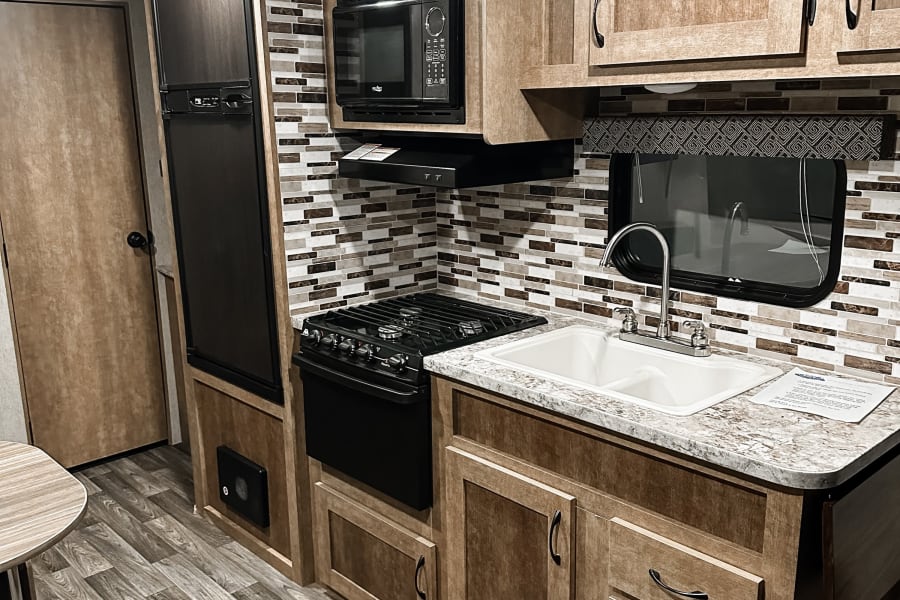 Inside an RV rental, a well-equipped kitchen features wood cabinets, stove, microwave, fridge, sink, and dining area.