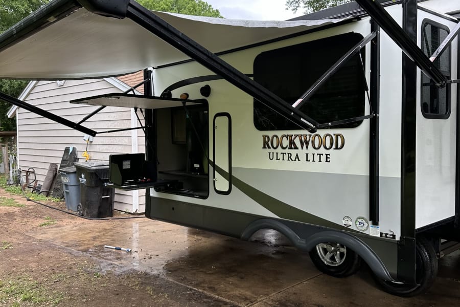 RV rental: Rockwood Ultra Lite travel trailer parked with awnings out, showcasing its outdoor kitchen setup.