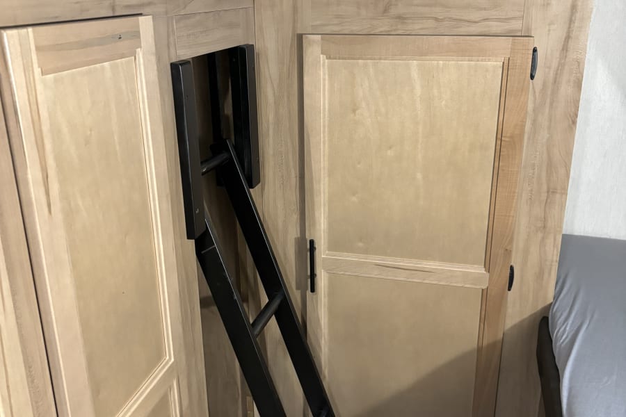 RV rental: Bunk bed, access ladder, and wood-look cabinets in a compact, comfortable RV interior.