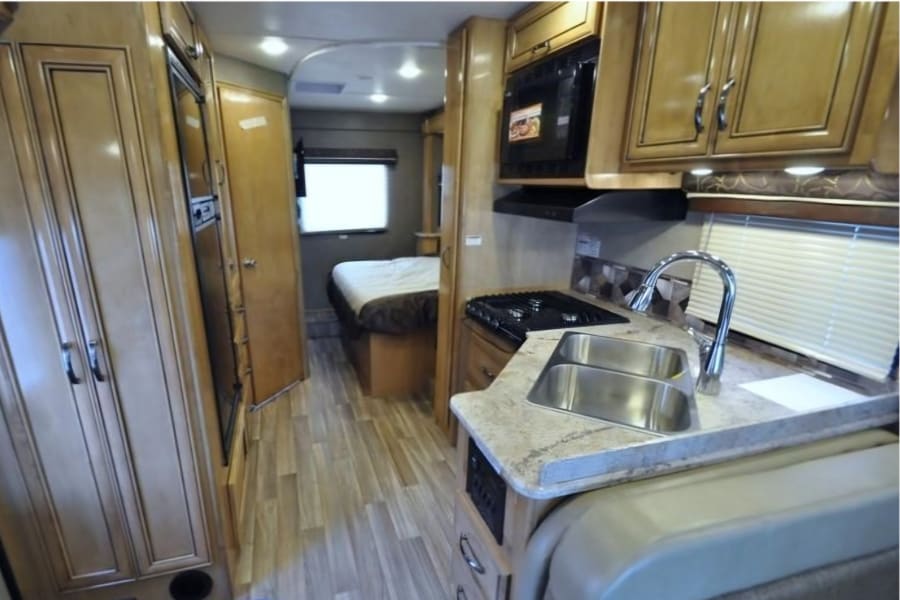 Inside this RV rental: a modern kitchen with double sink, stove, microwave, and a private bedroom with a comfortable bed.