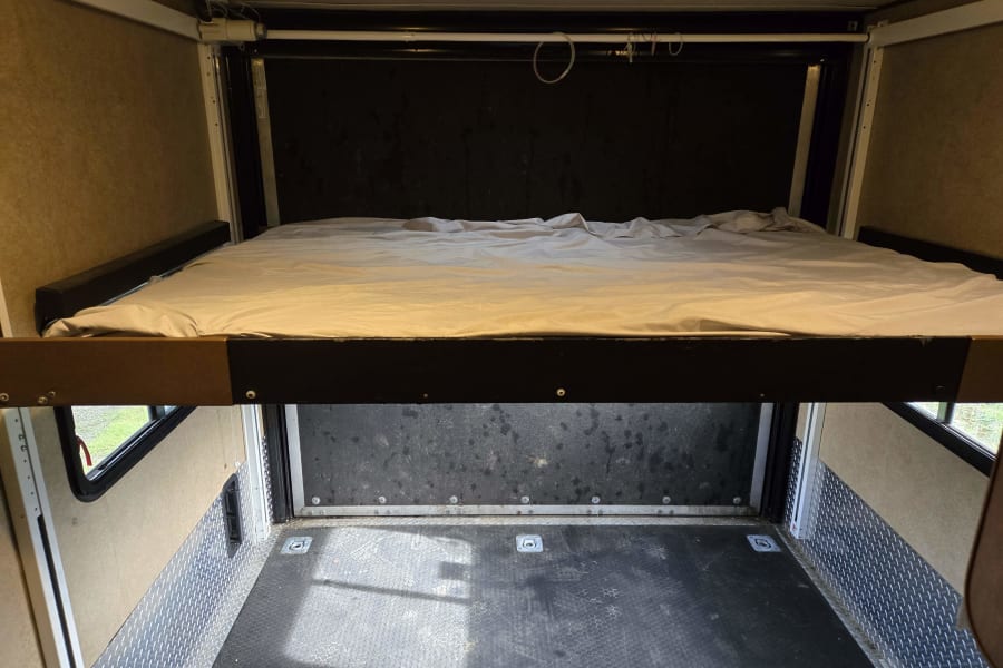 Toy hauler RV rental interior: A power-lift bed is raised, revealing the cargo area with durable flooring & tie-downs below.
