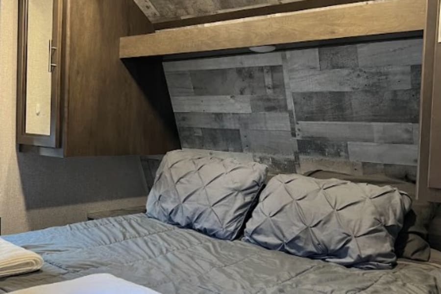 Comfortable RV rental bedroom featuring a bed with gray bedding, pillows, and stylish wood plank walls & ceiling.