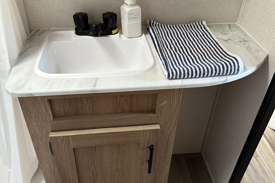RV rental bathroom with a white sink, black faucet, hand soap, and striped towel on a marble-look countertop.