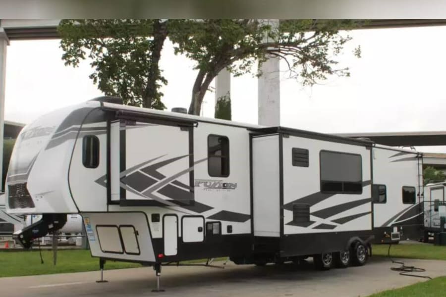 A large, modern white and black fifth-wheel RV with gray geometric graphics is parked outdoors, perfect for your next rv rental.