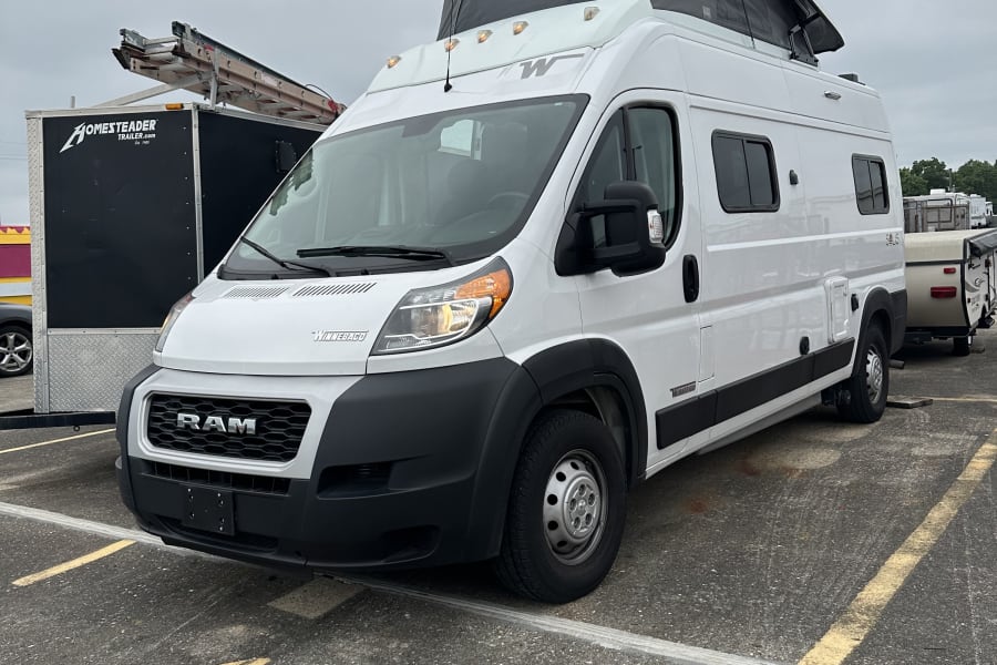 White Winnebago Solis pop-top RV rental (Ram ProMaster camper van) parked in lot 42 on a cloudy day.