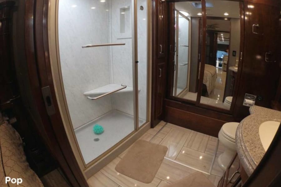 Spacious RV rental bathroom: glass shower, toilet, and vanity with mirrored reflections. Modern and clean motorhome interior.