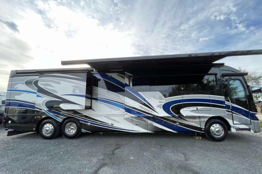 A sleek, blue, grey, and black Class A motorhome for rv rental, featuring extended slide-outs and awning, parked outdoors.